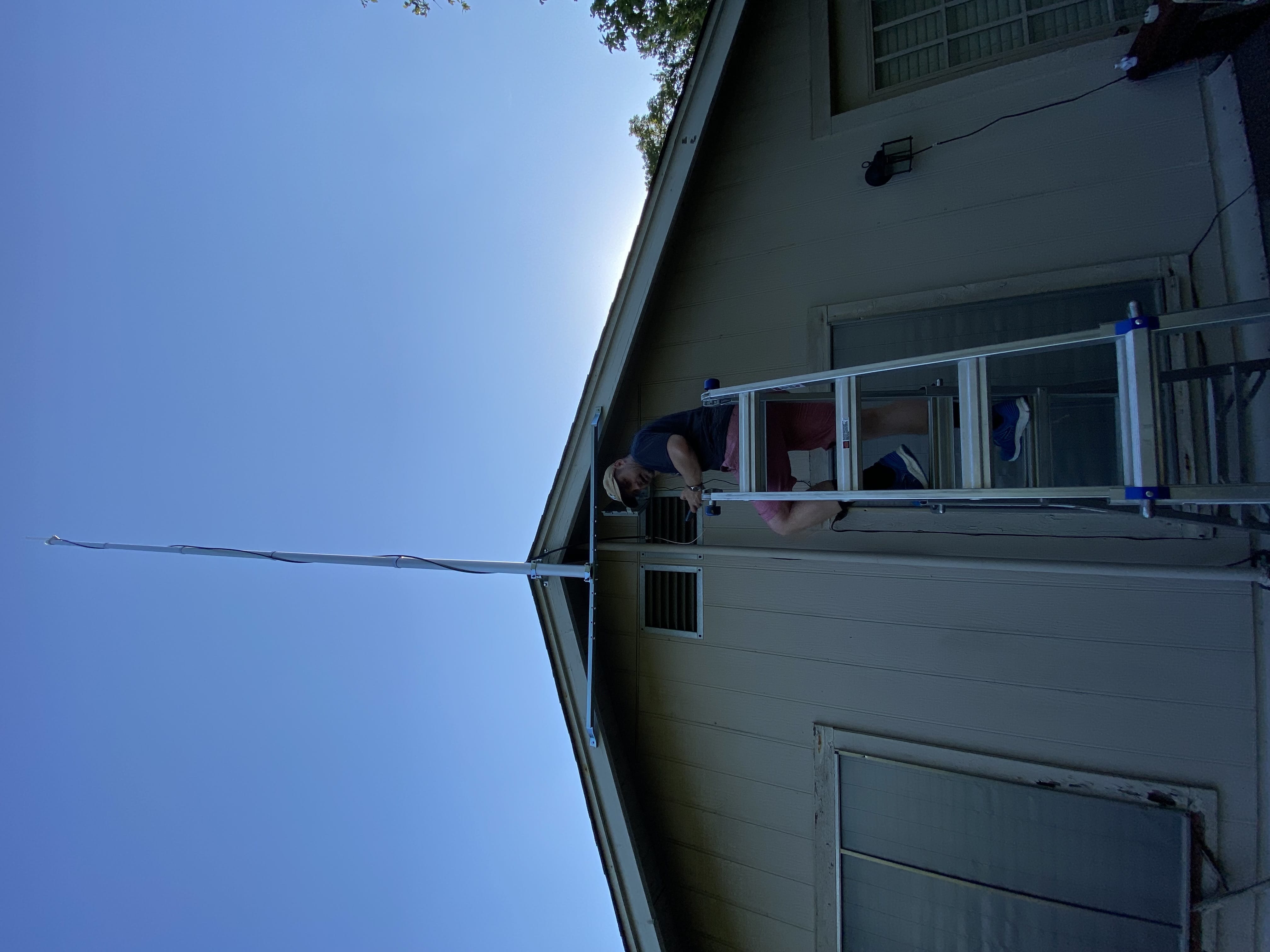 A guy on a ladder mounting a flagpole on his house