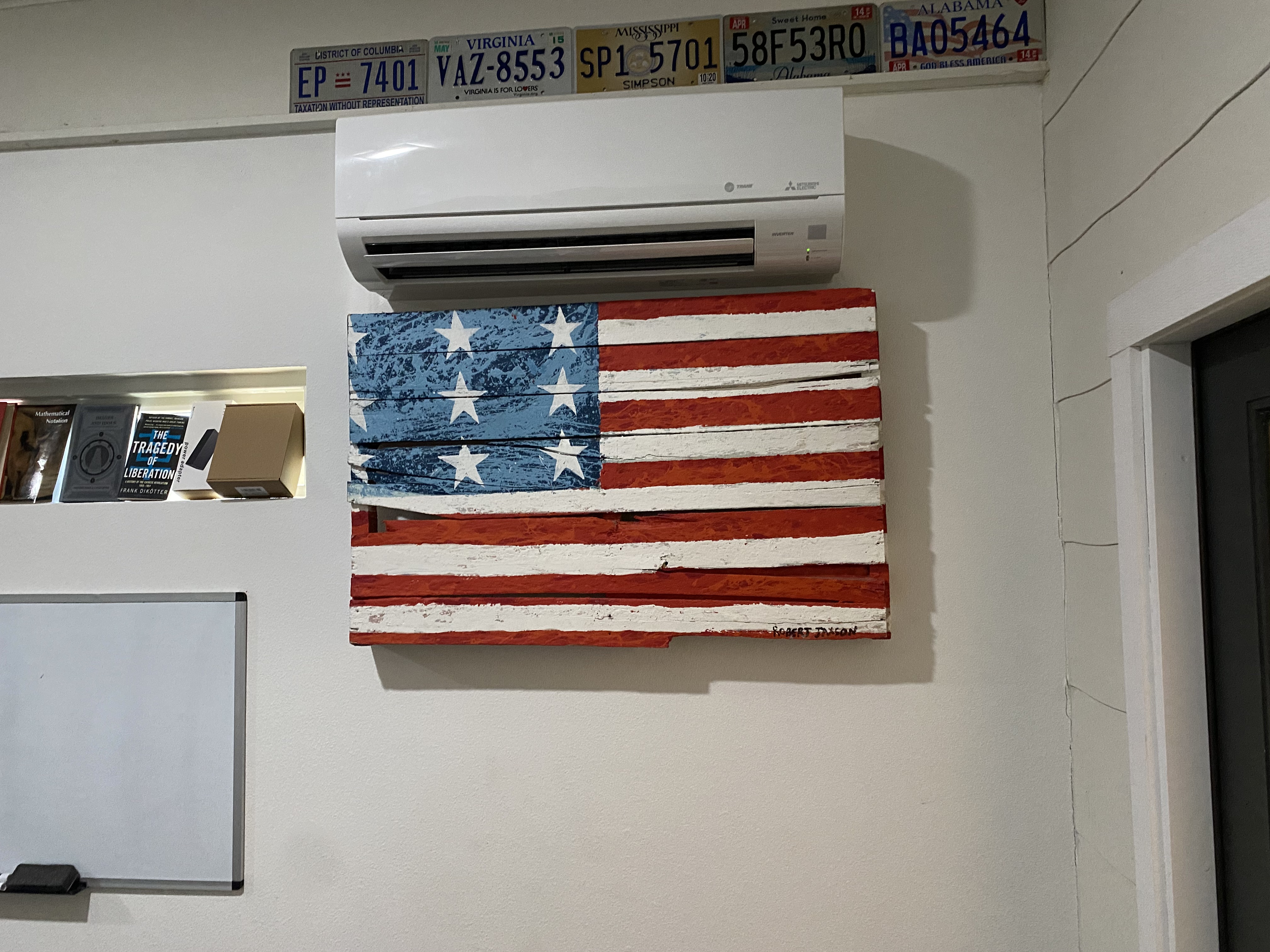 A ductless mini-split AC unit mounted to the wall, above an American flag painted on a wooden pallete.
